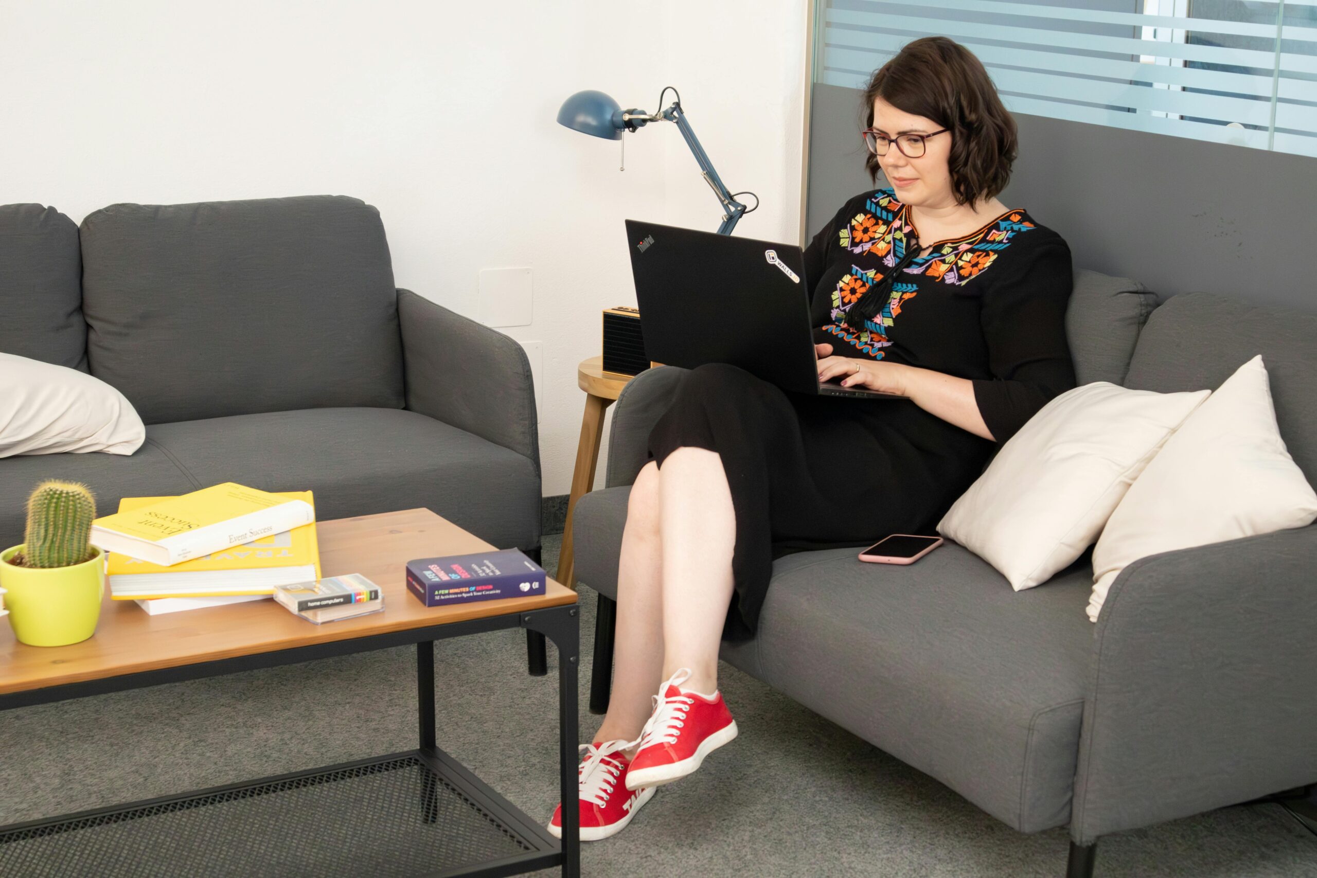 Junge dunkehaarige Frau sitzt auf einem Sofa und arbeitet.